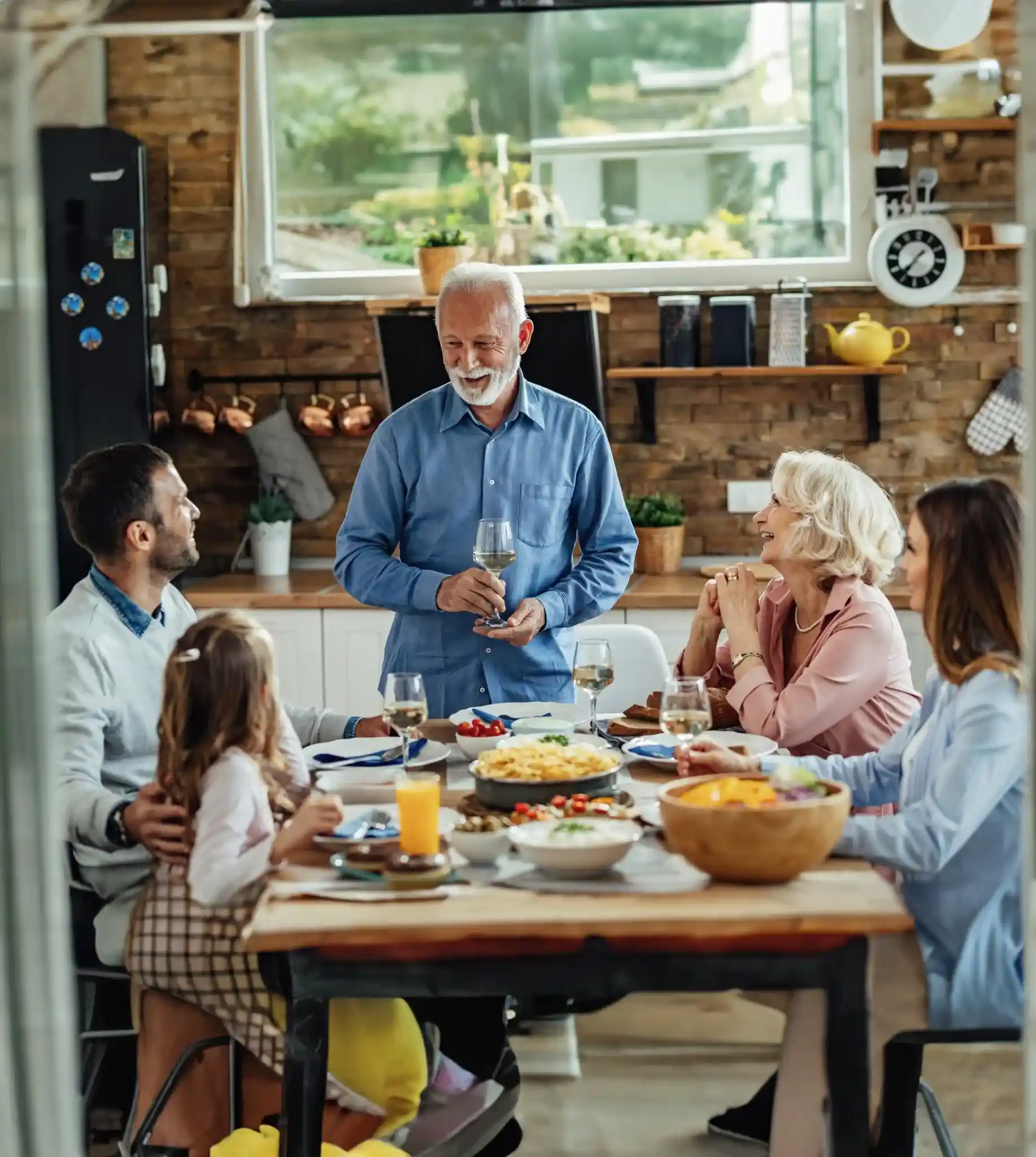 senior man standing at a dining table where the family is seated, enjoying a home-cooked meal