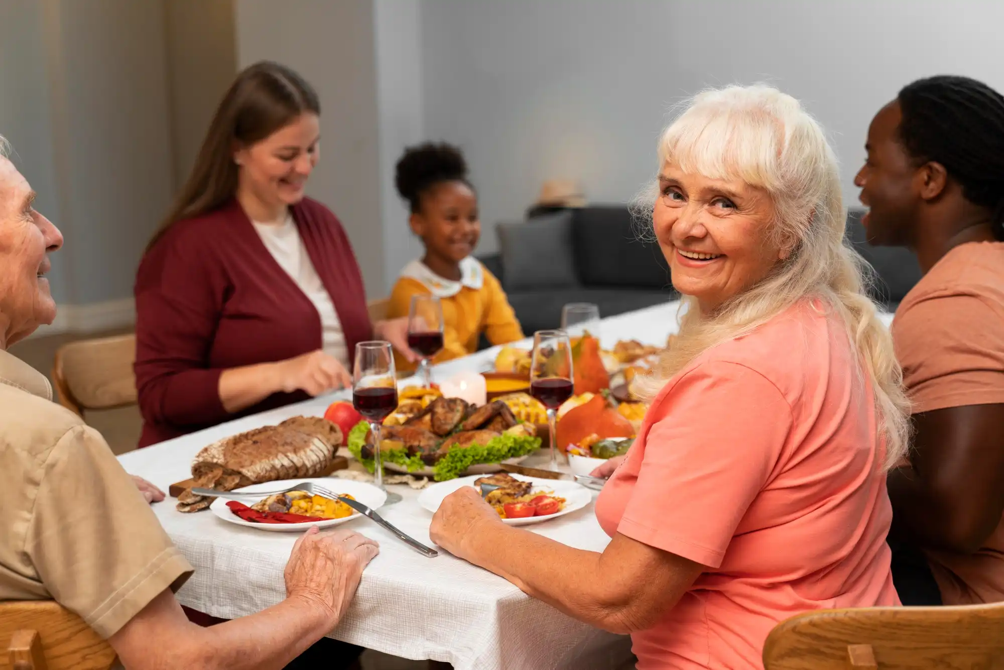 senior man standing at a dining table where the family is seated, enjoying a home-cooked meal